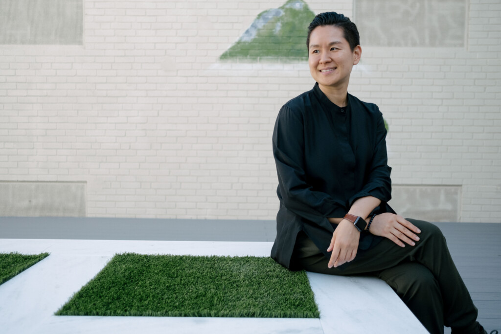 A woman in black seated on a white bench in a minimalist courtyard